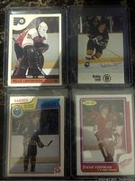 Four hockey cards including Pelle Lindbergh, Bobby Orr, Steve Yzerman, and Sabres player in protective sleeves on dark surface.