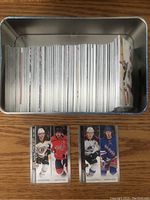 Metal tin box filled with a stack of white bordered NHL hockey cards from the 2020-21 Upper Deck series, with three cards displayed in front showing the front side images of players.