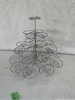 Photo of a three-tier metal cupcake or muffin tower stand with spiral holders, silver-colored, shown from the front on a plain background.