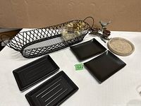 Photo showing black metal basket, four black dishes of different shapes, gel tea lights in clear containers, metal bird statue with two wood nests, and round planter dish.