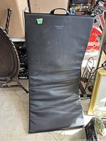 Front view of black full size exercise mat standing upright, showing general condition and carrying handle, with brand text visible.
