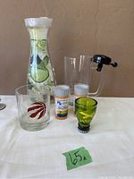 Photo shows all items: clear decanter with cucumber lime mint design, two prescription bottle style shot glasses, green Jamaica shot glass, Raptors logo shot glass, clear glass with black bicycle bell on handle.