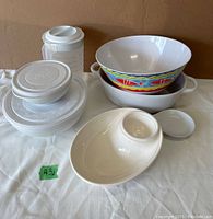 Kitchen bowls including two white Pampered Chef nesting bowls with lids, other white ceramic bowls, and colorful patterned bowl.