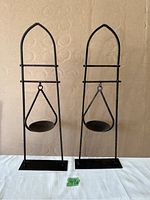 Front view of two tall metal candle holders with swinging candle dishes in a pointed arch frame.