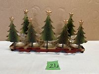 Front view showing all five green metal Christmas trees decorated with red dots and topped with gold stars, mounted on a red metal base with five clear glass tea light holders.