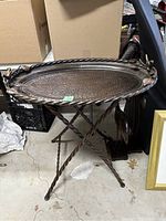 Side view of the metal bird bath showing the hammered oval basin, twisted metal legs, and decorative leaf accents along the edge.