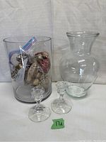 Clear glass vase, hurricane vase, and pair of candle holders visible together with decorative filler bag inside the hurricane vase.