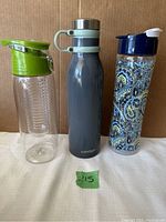 Full view of three water bottles in a row, including clear plastic infuser bottle, grey Contigo bottle, and patterned bottle.