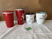 Four ceramic mugs, two travel mugs on the left, two traditional mugs on the right