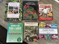 Top-down photo of 6 assorted books arranged together on a wooden surface including gardening and baking themes.