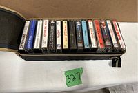 View of 11 cassette tapes inside the open black carrying case showing album titles and artists