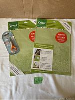 Two unopened Cricut adhesive cutting mats in original packaging and one opened 2-pack with one mat visible, laid flat on surface.