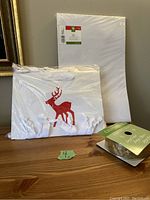 Photo of gift bags featuring white bags with red reindeer design and white handles, a white gift box, and gold ribbon spool.