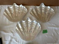 Three iridescent glass clam shell shaped plates shown stacked in a box wrapped in white fabric.