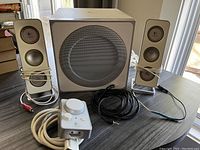 Front view of two satellite speakers, one subwoofer and remote control showing cables and condition.