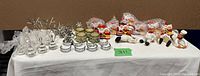 Photo shows a group of napkin rings and place holders arranged on a white surface including glass, metal, and ceramic pieces with holiday designs.