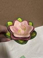 Front view of small ceramic flower-shaped candle holder, pink with hand-painted roses and green petals.