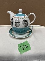 Tea for one set stacked showing teapot puckered on teacup and saucer, cupcake illustrations on teapot with turquoise lid and base with gold garland