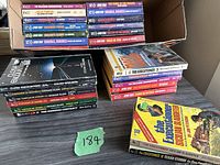 Overall collection of paperback books including Star Trek novels, The Executioner series, and others in a box and stacked on a table