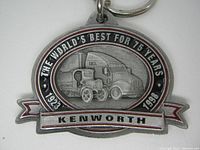 Front view of the Kenworth 75th Anniversary metal keychain showing embossed truck designs, anniversary dates, and branding.