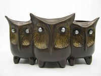 Front view of the ceramic planter showing the three owl faces with large gold-accented eyes and dark brown body.