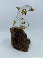 Front view of glass dolphin sculpture with gold highlights on wood burl base.