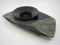 Angled front view showing black and greenish-gray speckled ceramic pottery Ikebana floral stand with built-in shallow bowl and metal flower-holding pins inside bowl.