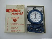 Stopwatch in original box showing front of box with branding and price sticker, stopwatch inside with blue cord coiled.