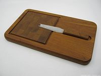 Full view of teak cutting board with wooden handled utensil in slot