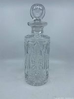 Front view of old cut crystal decanter with stopper, showing detailed cut designs and round faceted stopper with slight damage.