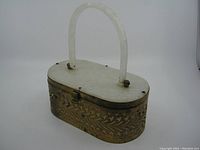 Front angled view of oval vintage purse showing metal decorative leaf cutout design and plastic handle with some rust on metal.