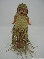 Front view of vintage celluloid Kewpie doll wearing woven grass skirt with long fringes, standing upright.