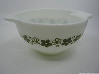 Front angled view of the white milk glass bowl with green flower designs around the exterior and pouring spouts