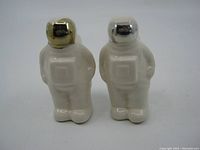 Front view of the two ceramic spaceman salt and pepper shakers showing one with a gold-colored helmet and one with a silver-colored helmet.