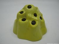 Yellow glazed mound-shaped flower frog with multiple holes, showing glossy finish and minor wear.