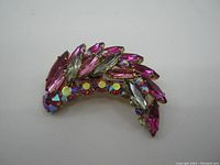 Photo showing front view of pink rhinestone brooch featuring marquise and round pink and clear stones, some aurora borealis finish, set in curved crescent shape.