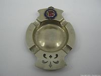 Top view of metal ashtray with RMS Queen Mary emblem badge and four cigarette rests.