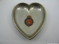 Top view of heart shaped metal dish showing the RMS Queen Mary enamel emblem in center with crown and red and blue flag design