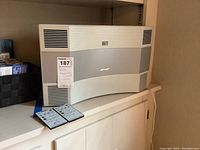 Front view of silver Bose Acoustic Wave Music System II with curved grille and two remotes placed in front