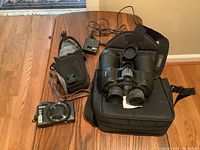 Nikon Coolpix camera, Nikon Action binoculars, their cases, and charger on wooden floor.