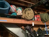 Wide shot of camping gear on shelving including sleeping bags, propane canisters, and other camping supplies.