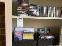 Photo showing multiple stacks of CDs and DVDs on shelves with some in black woven baskets