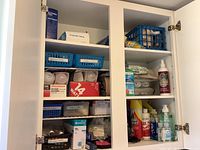 White cabinet containing lightbulb boxes, disposable gloves, hand sanitizer bottles, cleaning chemicals on two shelves