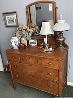Wooden dresser with attached mirror and items on top including two lamps and decorative objects