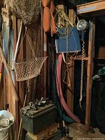 Overview of fishing rods leaning against wall beams, stacked tackle boxes on floor, nets and flotation items hanging