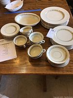 Wide view of the china pieces arranged on a wooden table, showing most of the plates, cups, saucers, and the serving bowl.
