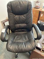 Front view of the large black vinyl office chair showing the padded seat, backrest, and armrests with some surface creasing and wear.
