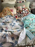 Full view of multiple handmade quilts layered on a full size bed with pillows and shams behind.