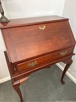 Front and side view of wooden secretary desk showing closed drop-down writing surface and brass hardware.