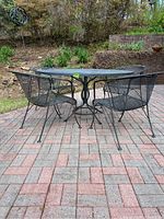 Set of round wrought iron table and four matching chairs setup outdoors on brick patio, showing overall condition and set composition.